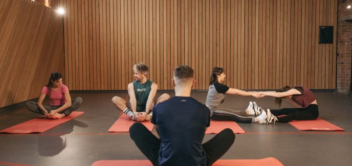 A group of adults practicing yoga and stretching on mats in a wooden panelled room.