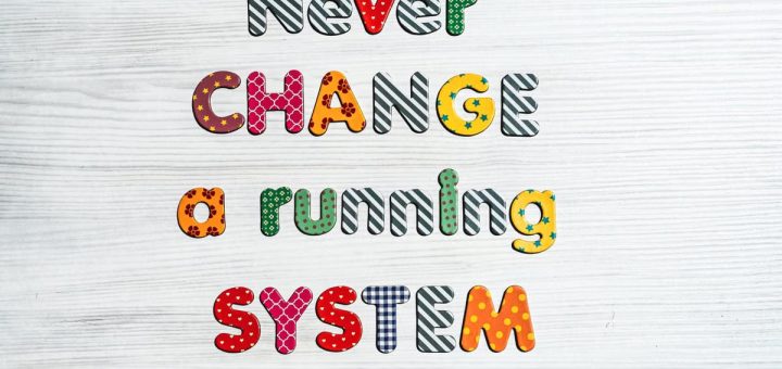 Inspirational quote "Never change a running system" in vivid letters on a wooden surface.